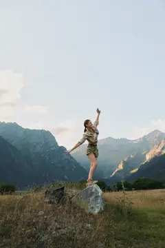 Молодая женщина раскинула руки на камне на фоне гор