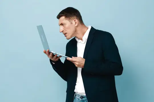 Удивлённый мужчина в пиджаке смотрит на ноутбук на голубом фоне
