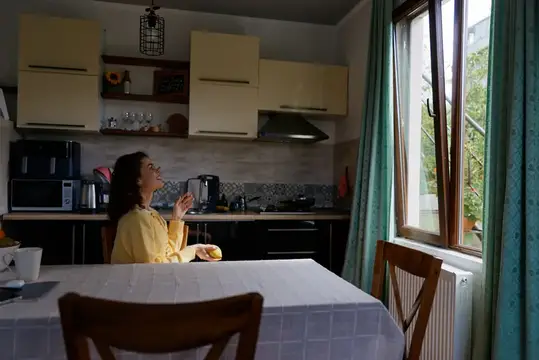 Яркий дневной свет струится через кухонное окно, пока задумчивая женщина наслаждается тихим моментом дома