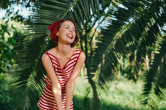 Радостная модель позирует среди пышных пальм, купаясь в теплом солнечном свете и ветреном настроении, передавая яркую, летнюю атмосферу, свободную от беспорядка, с естественным светом, зеленой…
