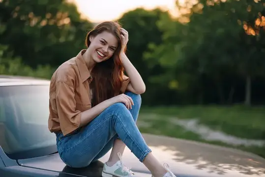 Рыжеволосая девушка смеётся, сидя на капоте автомобиля