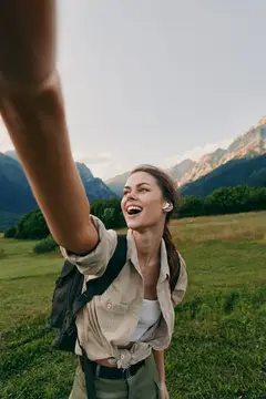 Смеющаяся девушка с рюкзаком делает селфи на фоне гор