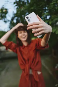 Смеющаяся девушка в красном платье делает селфи на телефон