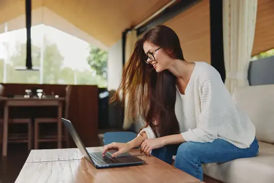 Улыбающаяся девушка в очках работает за ноутбуком в кафе