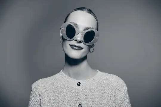Портрет молодой светлокожей женщины с зачёсанными назад волосами в oversized-круглых солнцезащитных очках и фактурном свитере