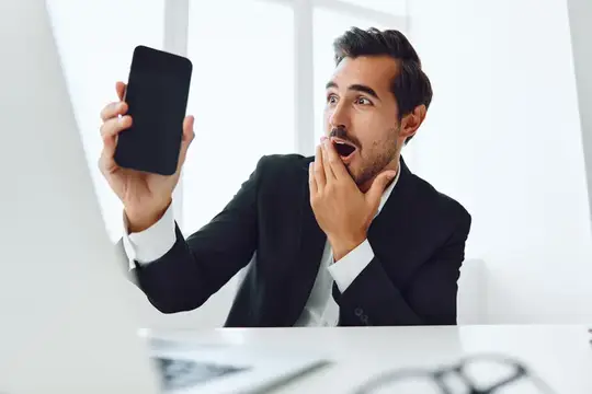 Удивлённый мужчина в костюме смотрит на смартфон в офисе