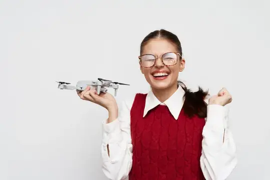 Улыбающаяся девочка в очках держит дрон на ладони