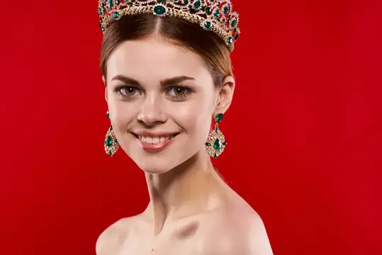 Улыбающаяся девушка в короне с изумрудами на красном фоне