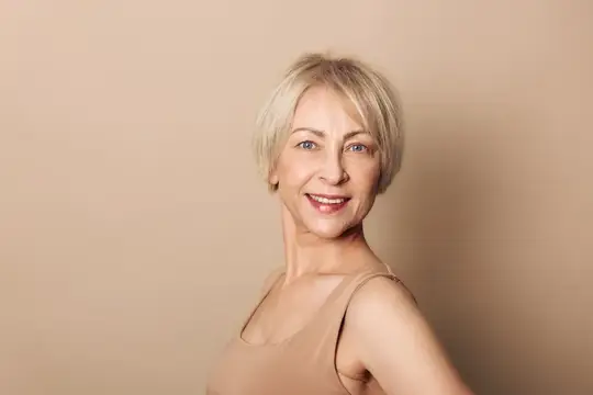Улыбающаяся блондинка в бежевом топе на бежевом фоне