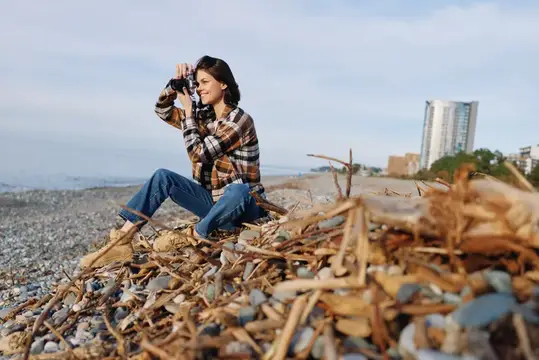 Девушка фотографирует на камеру, сидя на камнях у моря