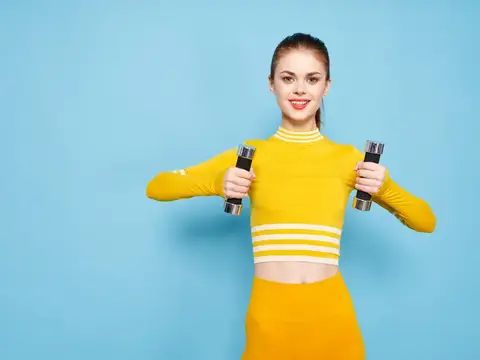 Спортивная девушка-модель с гантелями в руках на синем фоне