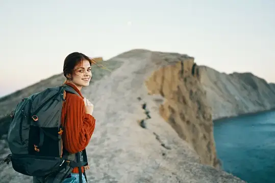 Улыбающаяся девушка с рюкзаком на фоне скал и моря