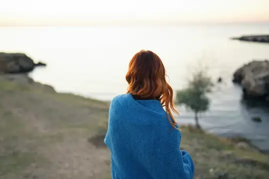 Рыжеволосая женщина в синем пледе смотрит на море