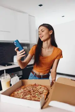 Молодая женщина фотографирует пиццу на телефон на светлой кухне