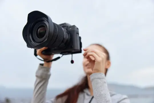 Веселая молодая женщина наслаждается фотографией на открытом воздухе, держа камеру и улыбаясь