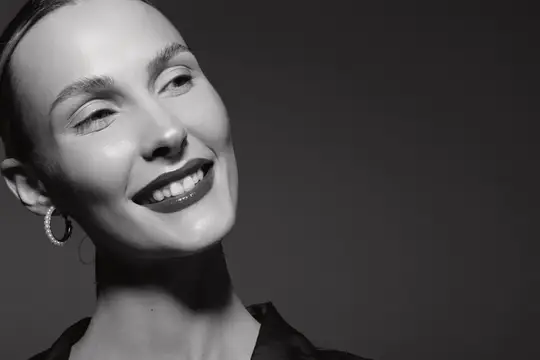 Улыбающаяся темноволосая женщина с серьгами на тёмном фоне