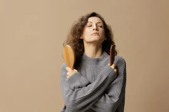 Кудрявая женщина с закрытыми глазами держит две расчески