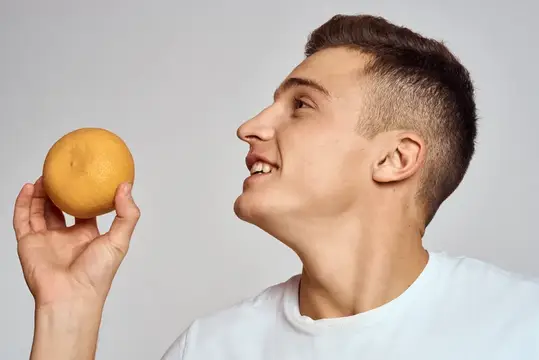 Мужчина с апельсином в белой футболке на светлом фоне
