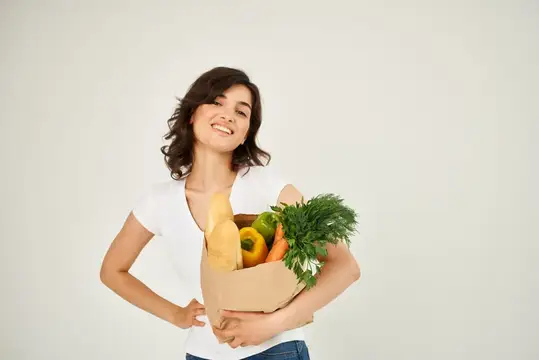 Жизнерадостная женщина в белой футболке с пакетом продуктов из супермаркета для здорового питания