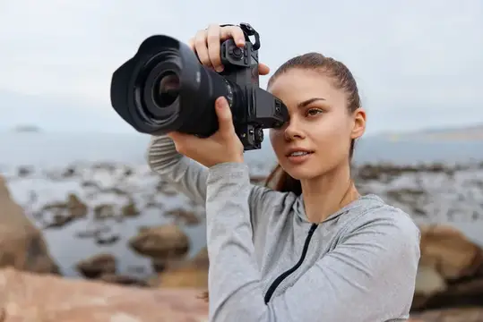 Молодая женщина фотографирует на камеру у скалистого берега