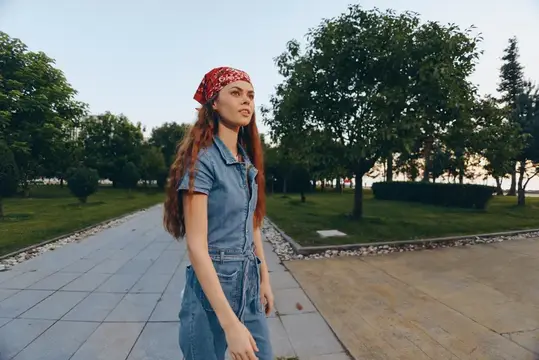 Женщина в стиле лайфстайл в современном бохо-вестерн джинсовом стритстайле уверенно идет по аллее, одетая в красную бандану и джинсовый наряд