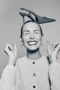 Улыбающаяся женщина с туфлей на голове держит пальцы скрещенными