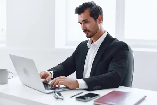 Сосредоточенный темноволосый мужчина в костюме работает за ноутбуком в офисе