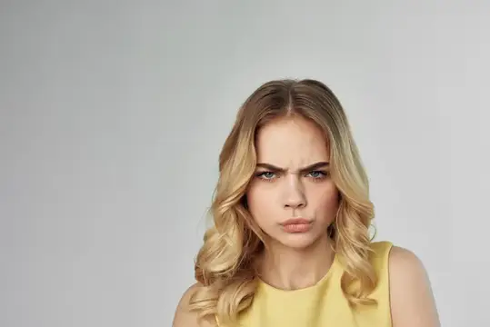 Недовольная блондинка с нахмуренными бровями на сером фоне