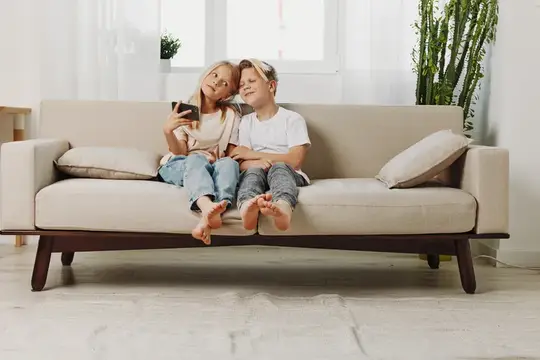 Брат и сестра сидят на диване и смотрят в смартфон