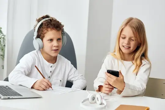 Кудрявый мальчик в наушниках и девочка со смартфоном за столом