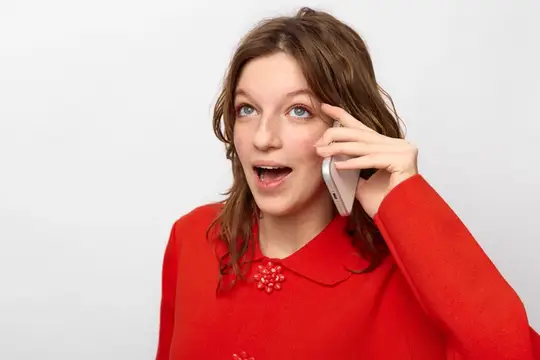 Удивленная молодая женщина в красном свитере прижимает смартфон к уху