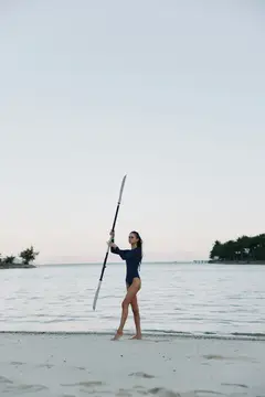 Девушка с веслом стоит на песчаном берегу у спокойной воды