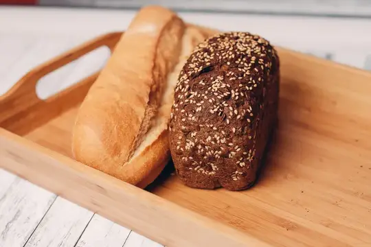 Белый багет и ржаной хлеб с семечками на деревянной доске