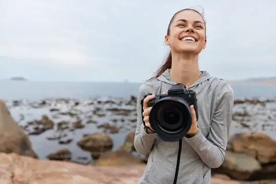 Улыбающаяся девушка с фотокамерой на берегу моря