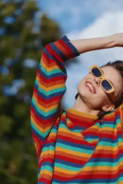 Улыбающаяся девушка в солнечных очках и радужном свитере на фоне неба