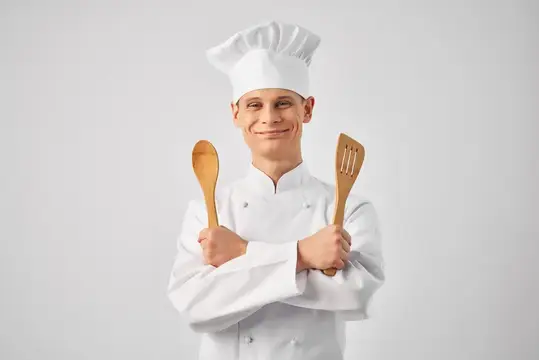 Улыбающийся повар в белом колпаке с деревянными лопатками
