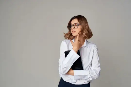Задумчивая девушка в очках с блокнотом на сером фоне
