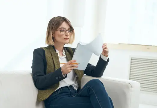 Женщина в очках с блокнотом и карандашом сидит на диване