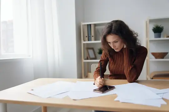 Восхитительная серьёзная задумчивая кудрявая милая леди сидит за столом с бумагами и документами, работая из дома, размышляет о провале бизнеса или банкротстве, рассчитывает бюджет, держит ручку…