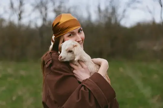 Женщина мягко улыбается, когда козленок прижимается к ней, демонстрируя деревенское очарование, свежий воздух и искренний момент товарищества в мирной сельской обстановке