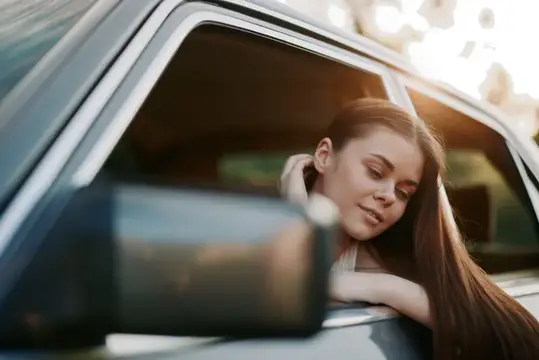 Молодая женщина с длинными волосами выглядывает из окна автомобиля