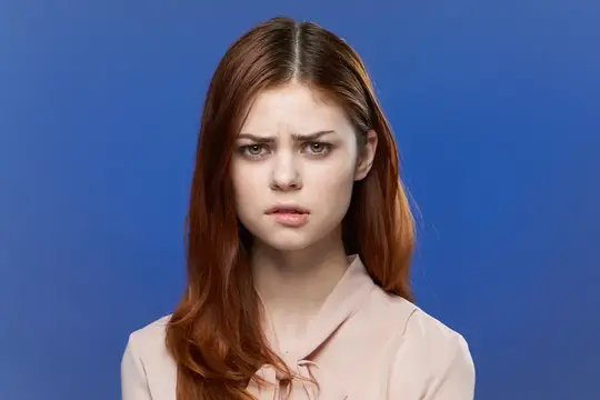 Рыжеволосая девушка с недовольным выражением лица на синем фоне