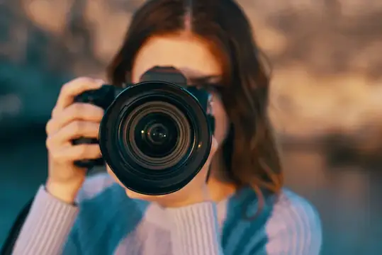 Рыжеволосая женщина с фотоаппаратом на природе в горах возле реки