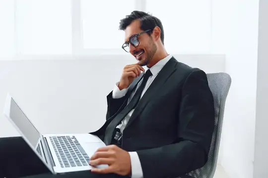 Улыбающийся мужчина в костюме и очках работает за ноутбуком