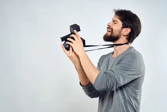 Бородатый мужчина со смехом держит фотокамеру на вытянутых руках