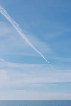 Белый след самолёта в ясном небе над морем