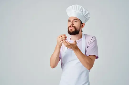 Бородатый повар в колпаке показывает жест пальцами