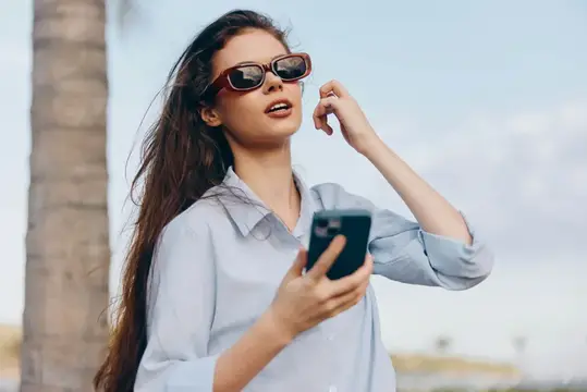 Молодая женщина в солнцезащитных очках смотрит в смартфон на улице