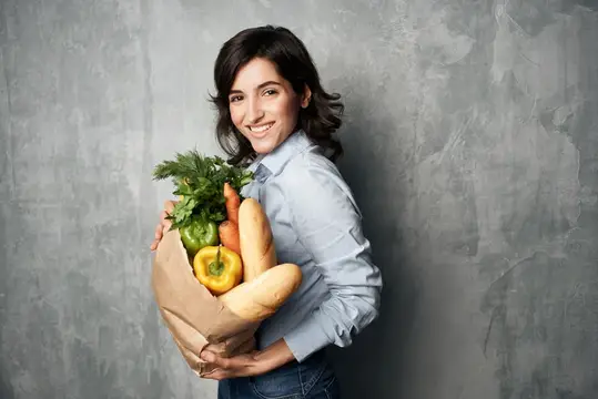 На фотографии высокого качества изображена женщина с пакетом продуктов, покупающая овощи