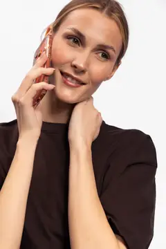 Молодая улыбающаяся женщина прижимает смартфон к уху, задумчиво глядя в сторону